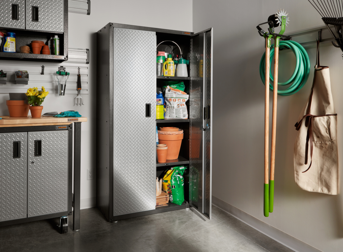 An opened Gladiator unit in a garage, holding various gardening supplies. There are two more Gladiator Modular Cabinets with plants on top, and a GearTrack System holding gardening tools and a garden hose. Gardening tools hang on the wall above one of the cabinets.