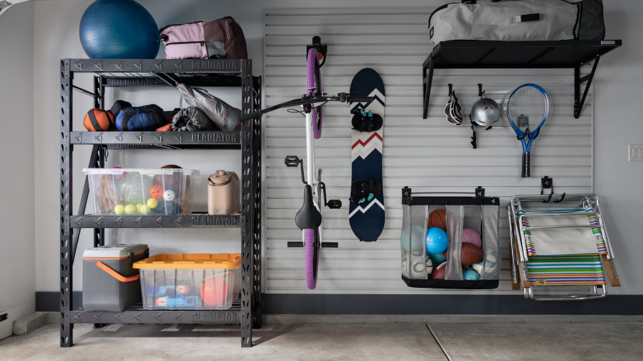 Un garage bien organisé. Un vélo, une planche à neige et des raquettes de tennis sont accrochés à des crochets muraux Gladiator. On voit aussi une unité de rangement Gladiator contenant un ballon d'entraînement, un bac rempli de ballons et d’autres articles. Près du sol, on voit un panier Gladiator rempli de ballons et des chaises pliantes suspendues à des crochets muraux Gladiator.