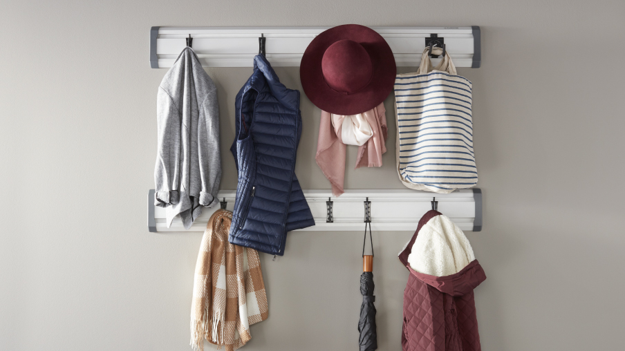 Des vêtements comme un chapeau, un chandail à capuchon et un manteau sont suspendus à un système Gladiator GearTrack sur un mur.