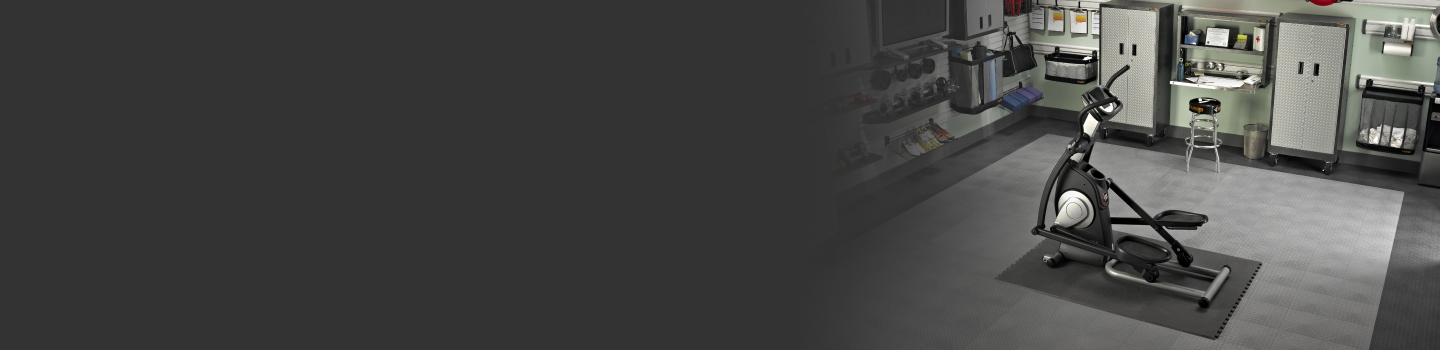 Un garage aménagé en salle d’entraînement à la maison. On y voit un elliptique. Les articles autour du garage sont bien organisés dans des systèmes de rangement Gladiator, comme des unités de rangement, des armoires, des paniers et plus.