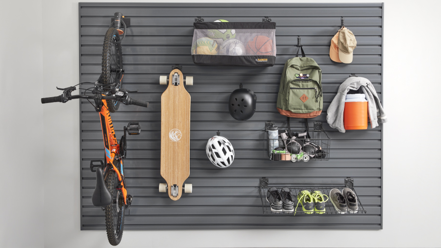 Hanging on Gladiator hooks and in Gladiator baskets on a wall are a skateboard, a bicycle, helmets, a backpack, hats, shoes, and a water cooler. 