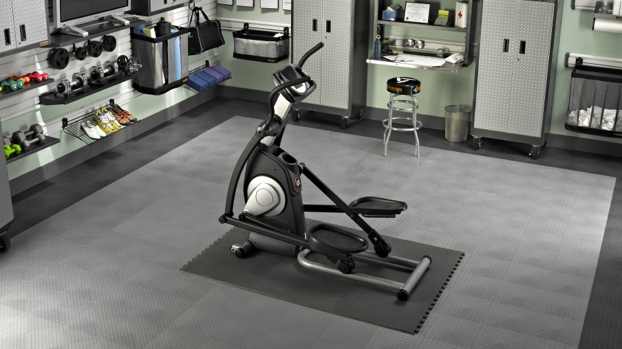 A home gym with an elliptical in the centre of the room. Gladiator storage solutions, like Gladiator cabinets and Gladiator storage units, are in use along the walls to organize items. 