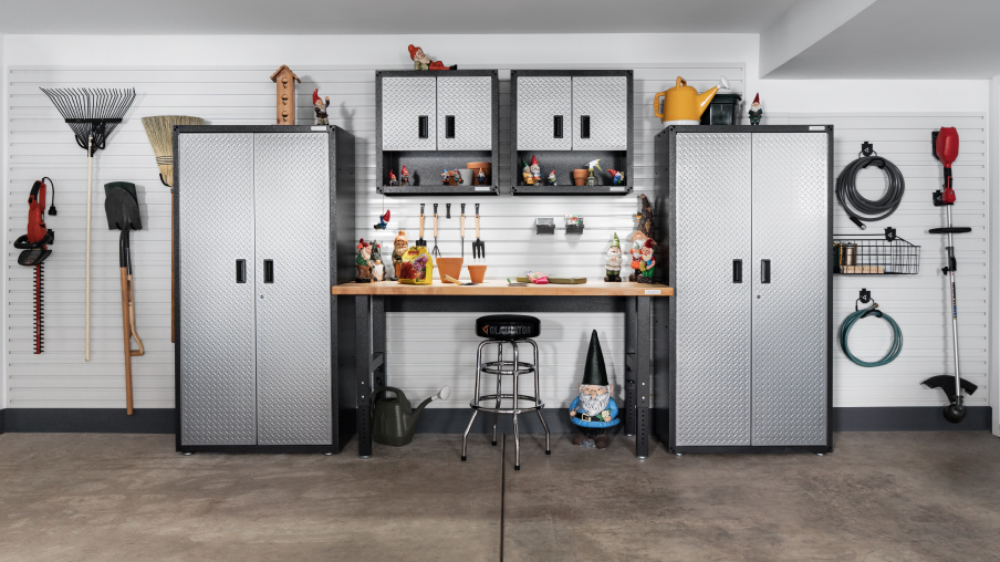 Un mur de garage avec deux unités de rangement Gladiator et deux armoires Gladiator. Des outils de jardinage, des boyaux et des paniers Gladiator sont accrochés au mur