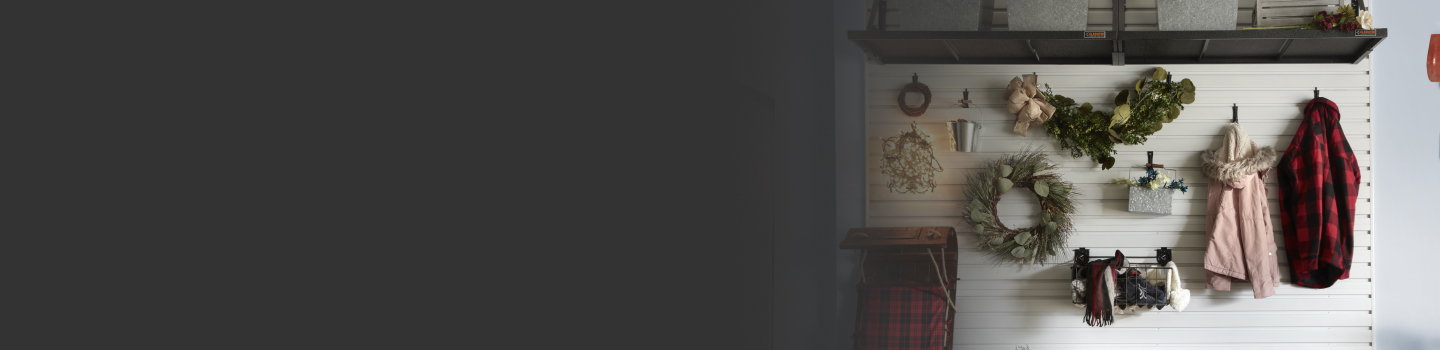 Sur un mur, deux manteaux, deux couronnes de Noël et des tuques d'hiver sont organisés sur des crochets muraux Gladiator et rangés dans un bac Gladiator. Une luge est appuyée contre le mur à côté des articles suspendus.