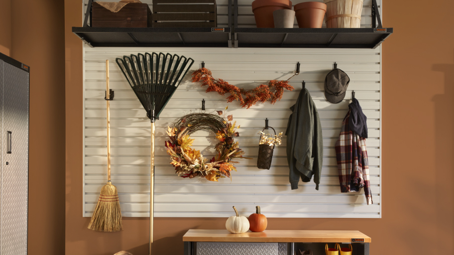 Des articles saisonniers comme un râteau, des manteaux et des couronnes de Noël sont rangés sur des crochets muraux Gladiator. Au-dessus des articles suspendus se trouvent des tablettes avec des pots de plantes, et en dessous, un meuble à chaussures Gladiator.