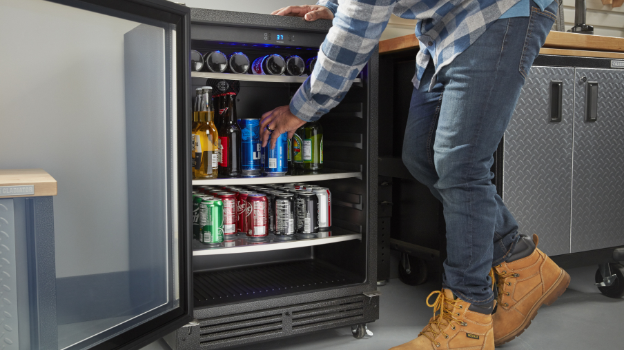 Une personne portant des bottes de travail sort une boisson en canette d’un centre de boissons situé à côté d’une armoire Gladiator sur roulettes.