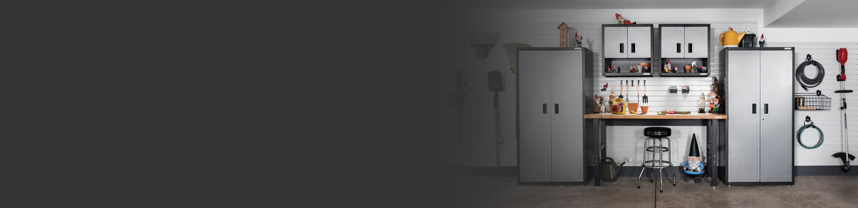 Le mur d’un garage avec des systèmes de rangement Gladiator. On voit des armoires Gladiator, des unités de rangement Gladiator et un établi Gladiator. Des outils de jardinage et d’autres articles sont suspendus au mur
