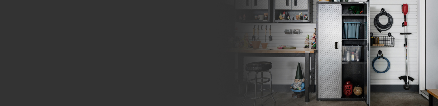 Une unité de rangement Gladiator avec la porte ouverte. À l’intérieur se trouvent des bacs, une bonbonne de propane et d’autres articles. À côté se trouvent un établi Gladiator avec un tabouret. De l’équipement de jardinage est accroché au mur à l’aide de crochets Gladiator.