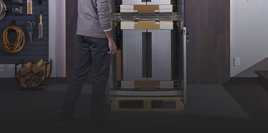 Someone stands in front of a Gladiator Cabinet. Nearby is a basket of logs. On the wall, hanging on hooks, are rope, shears, a brush and a level. There are also two bins hanging on the wall