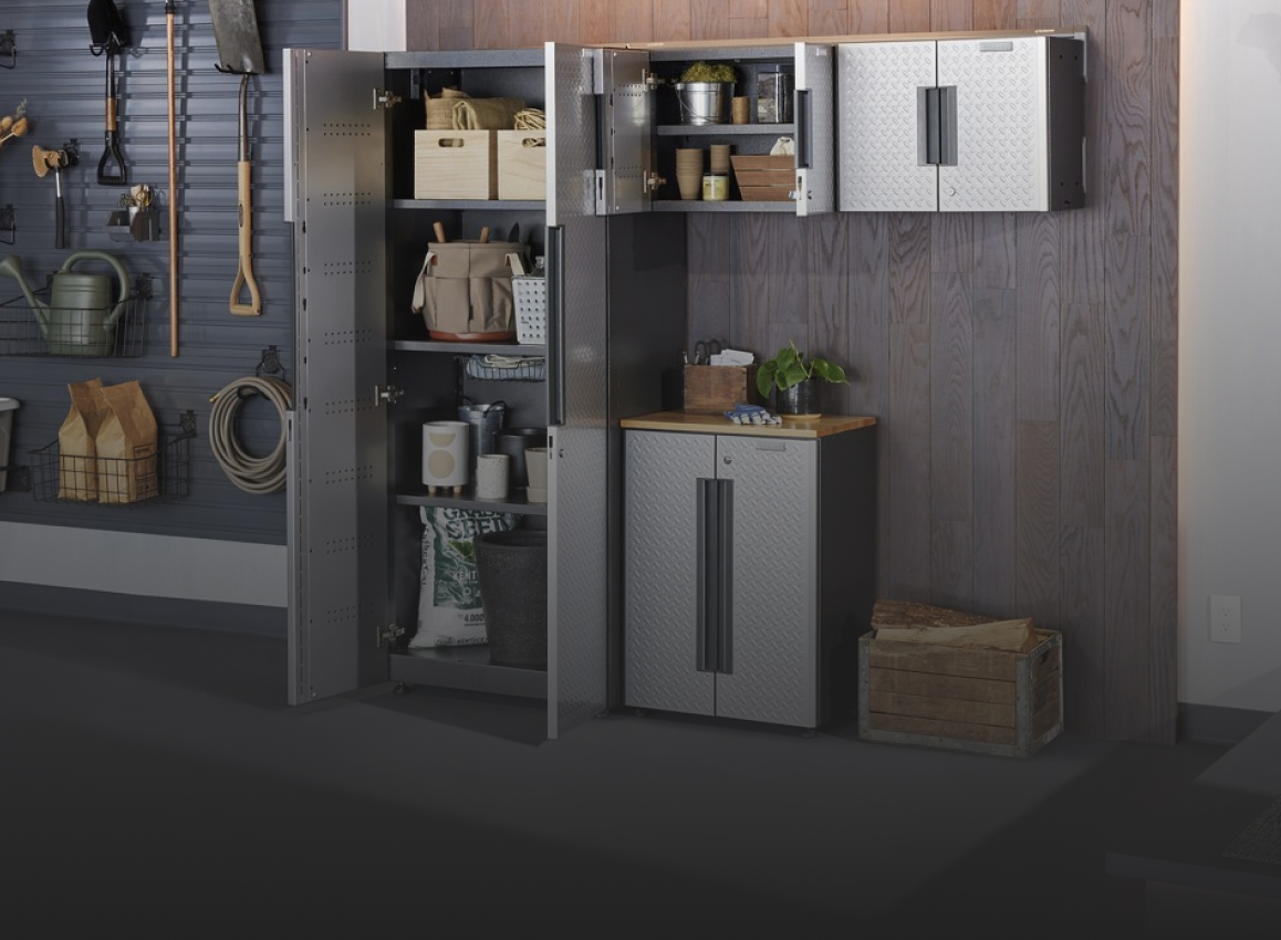 A garage with a Gladiator Flex Cabinet System. The vertical cabinet doors are opened revealing a toolbox, baskets, paint cans, a bag of soil and other various items. One of the top cabinets is also opened and on the shelves are baskets, a metal container and more