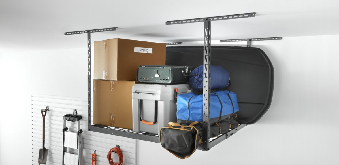 A Gladiator Overhead Storage holding two boxes, a grey bin, a sleeping bag, a blue bag, a black bag and a long black board.