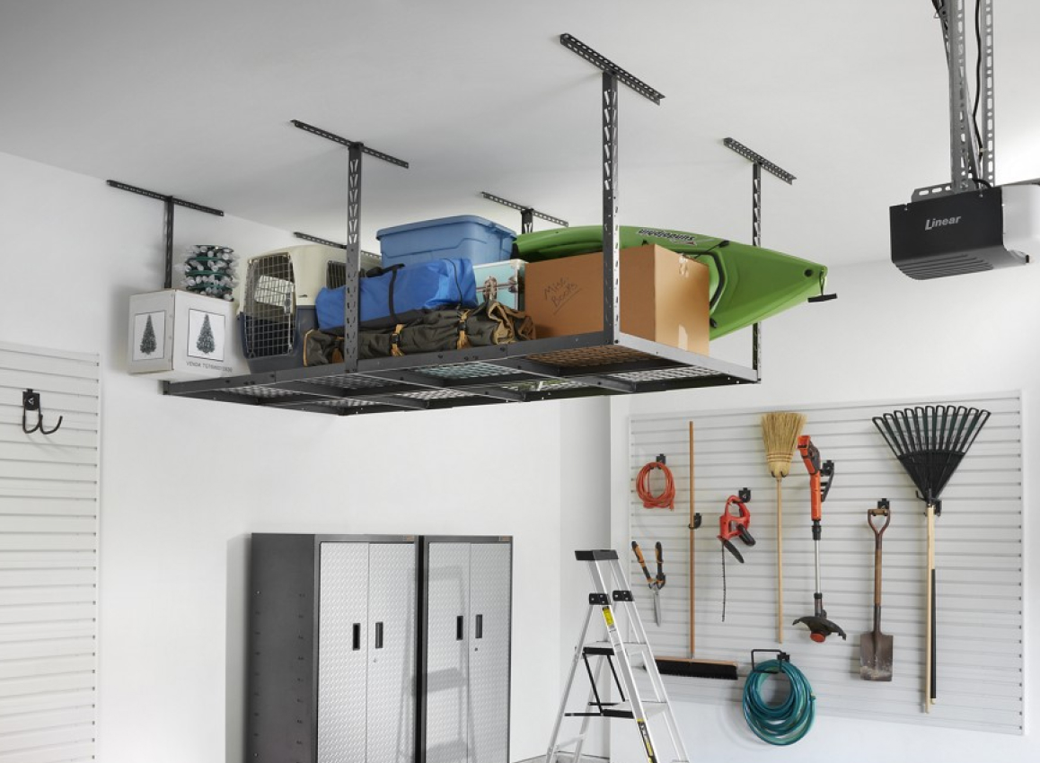 A garage with Gladiator Overhead Storage holding a box, kayak, bags, bins and more. There's also a Gladiator GearBox, ladder and gardening tools hanging on the wall on Gladiator Hooks.