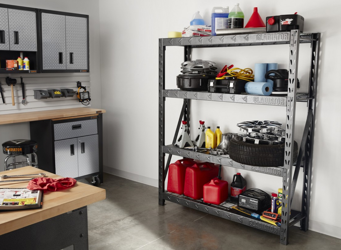 A garage with a Gladiator Shelving Unit. On the shelves are paper towel rolls, jerry cans, tires, rims, car fluids, jumper cables and more. There's also Gladiator Modular Cabinets, a stool and the corner of a workbench. Tools and bins hang on the wall.