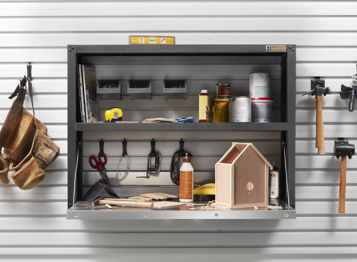 On a wall, hanging on Gladiator Hooks are a toolbelt, mallet, hammer and another item. In a Gladiator Shelving Unit are an almost completed birdhouse, glue, scissors, bins, cans, tape measure and more