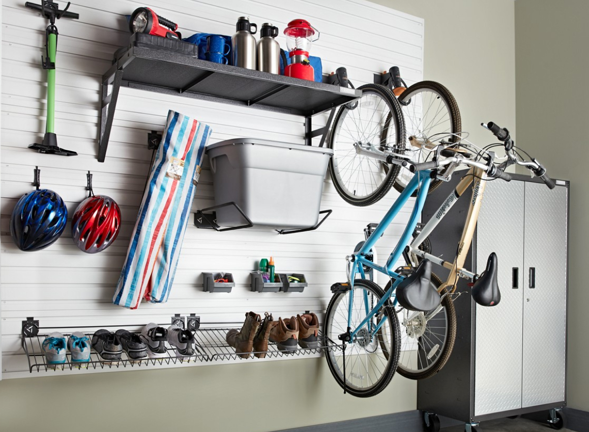 Hanging on a Gladiator GearTrack system are an ice scrapper, bike helmets, a bin, shoes, boots, two bicycles and a shelf with various items like a bug zapper. Next to the GearTrack is a Gladiator Full-Size Cabinet