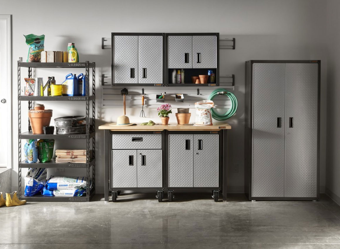 A garage with Gladiator Modular Cabinets, a Gladiator Workbench and a Gladiator Rack Shelving. The rack shelving is filled with gardening items like plant pots, bags of soil, yard waste bags and more. On the modular cabinets are a sun hat, potted plants, a bag of soil and more. Hanging on the wall are gardening tools and a garden hose