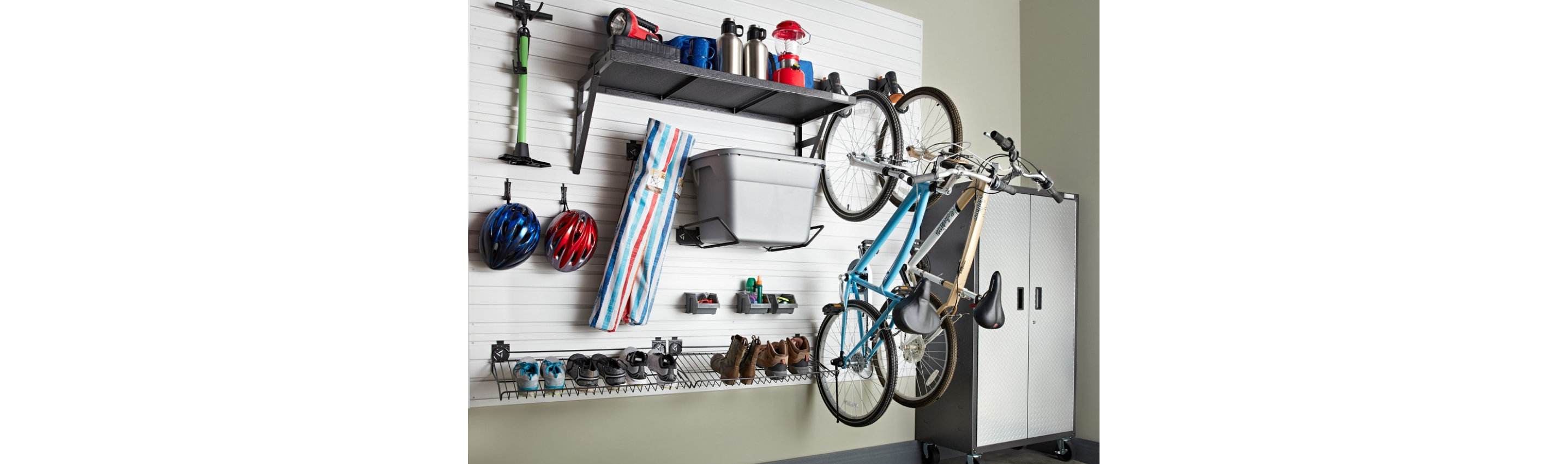 Hanging on a Gladiator GearTrack system are an ice scrapper, bike helmets, a bin, shoes, boots, two bicycles and a shelf with various items like a bug zapper. Next to the GearTrack is a Gladiator Full-Size Cabinet