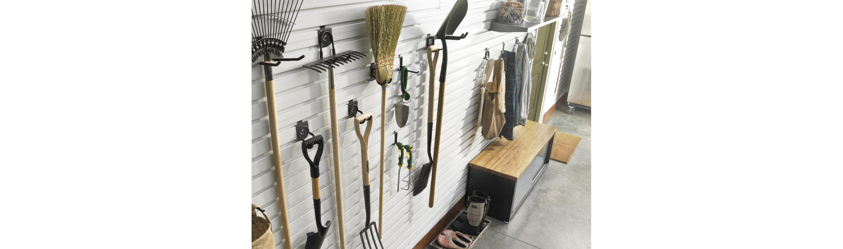 Hanging on a Gladiator GearTrack system are gardening tools like a rake and shovels, among other items. Nearby, aprons hang above a Gladiator Storage Shoe Bench and below a shelf of items