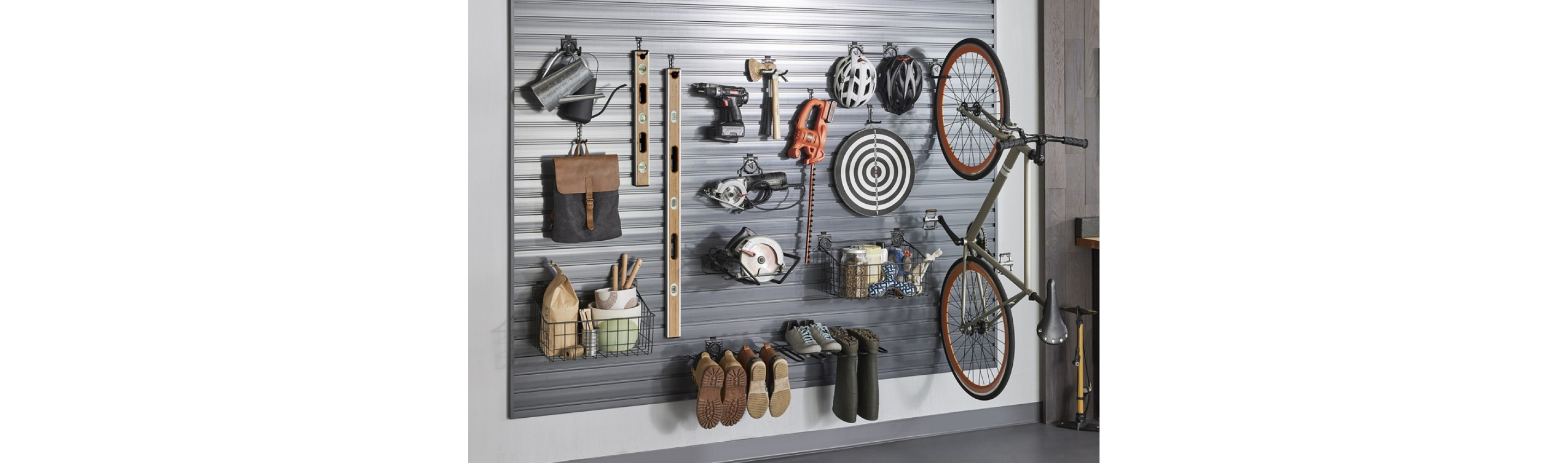 Hanging on a Gladiator GearTrack system are a watering can, a bag, a basket with items, two levels, tools like drills, shoes, boots, a bullseye, bike helmets, a bike and another basket filled with items